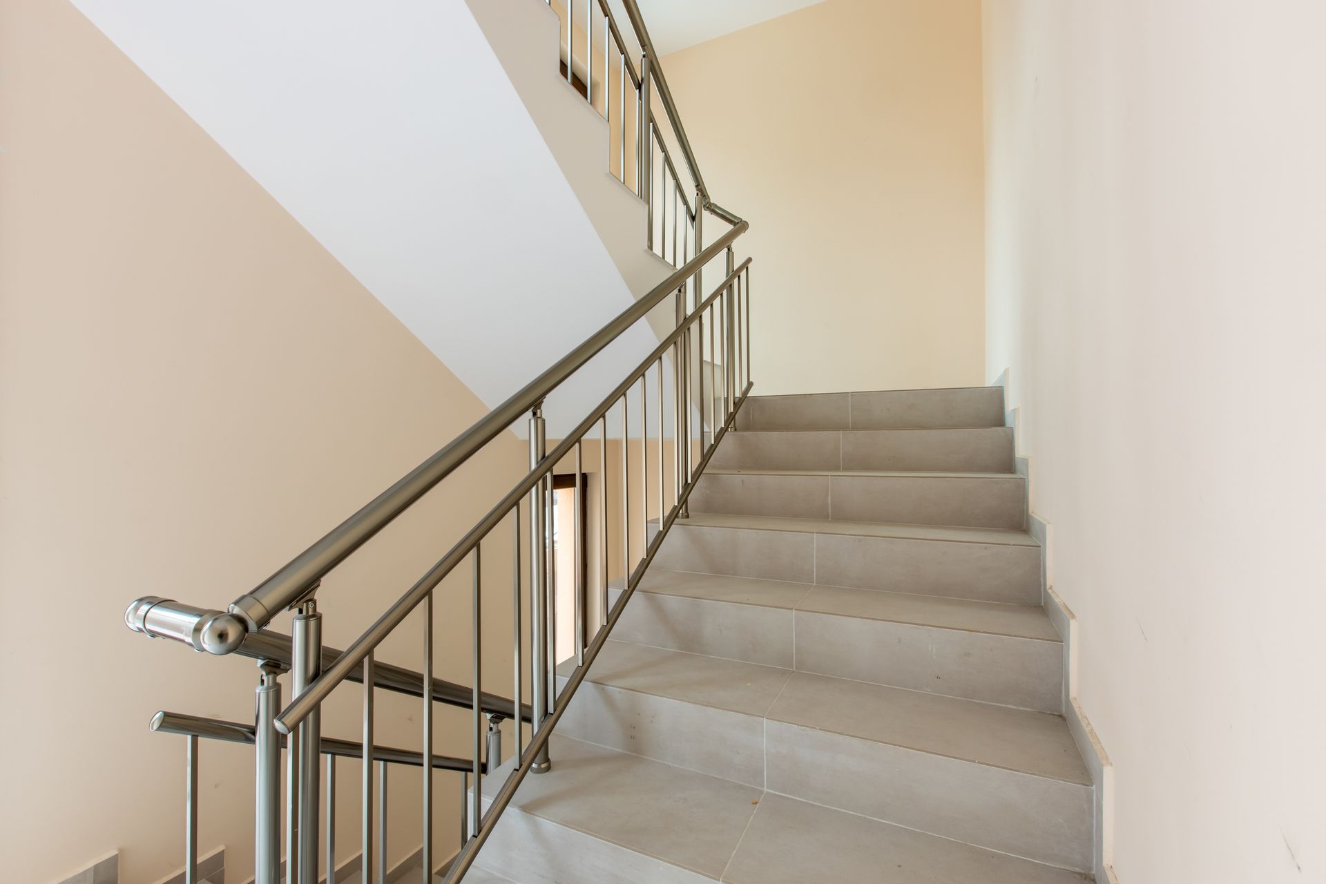 Un escalier intérieur en pierre avec une rampe en métal menant vers le haut entre des murs beiges.