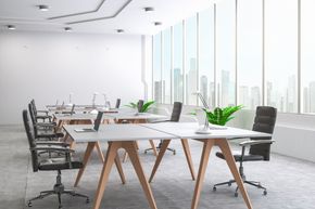 Un espace de bureaux moderne et minimaliste avec des rangées de bureaux blancs sur des pieds en bois en forme de A, des chaises ergonomiques et une vue sur la ville.