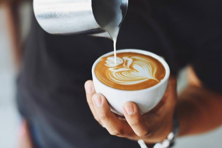 Latte art being poured into a white cup held in hand