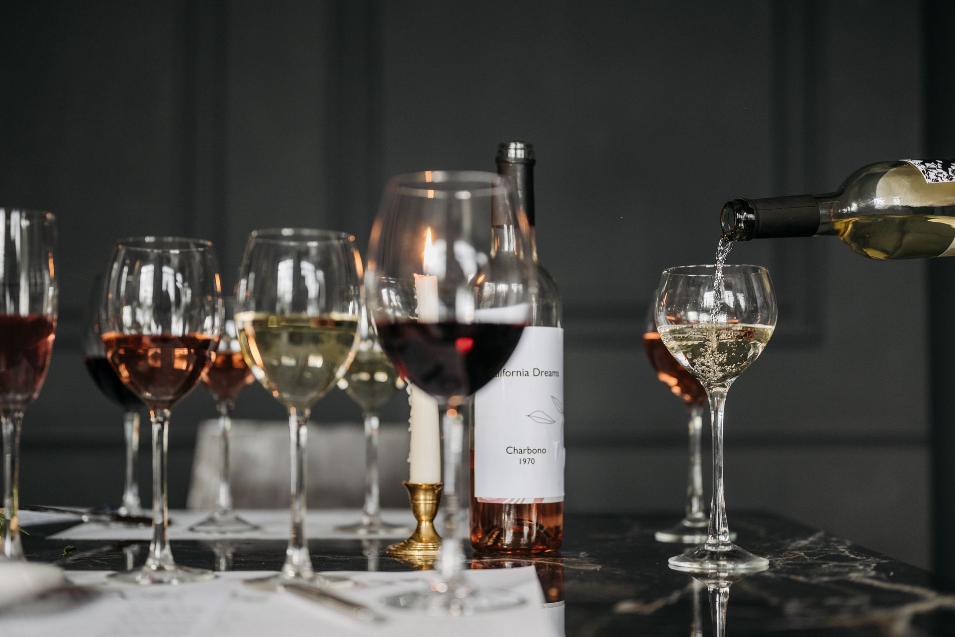 Wine bottles and glasses on a table, with red and white wine being poured in a dimly lit setting