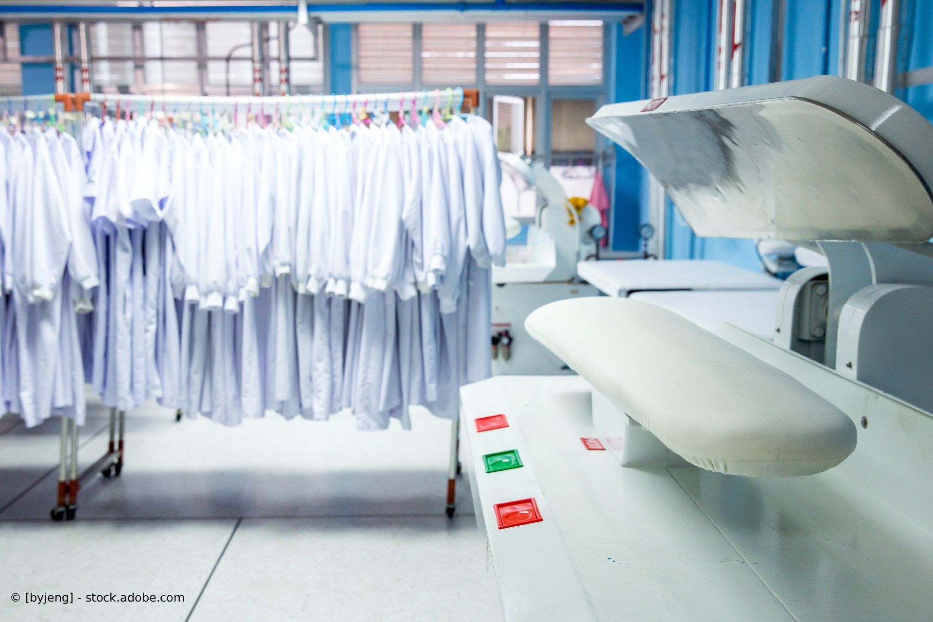 Waschküche mit hängenden weißen Hemden und einem großen Industriebügeleisen.