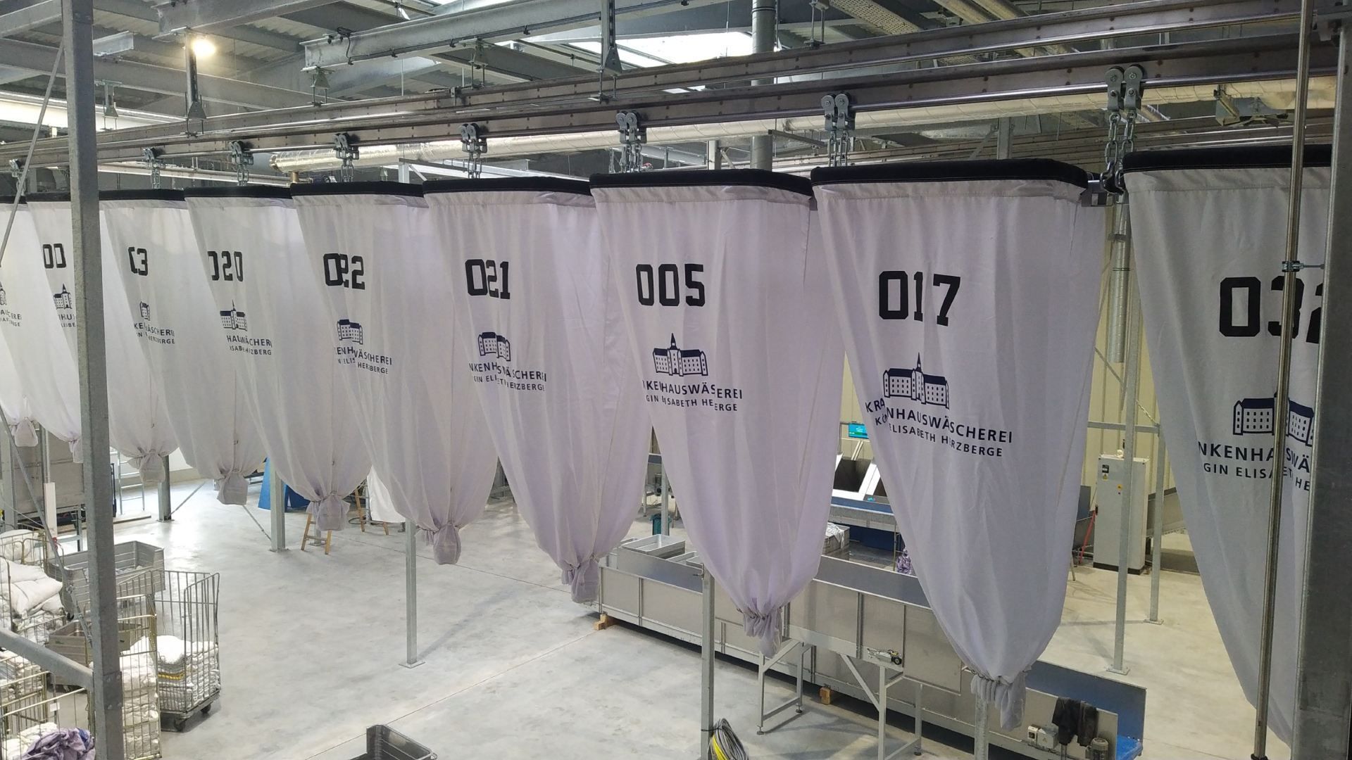 Weiße Stoffsäcke mit Nummern hängen an einer Schiene und dienen vermutlich der Wäschesortierung