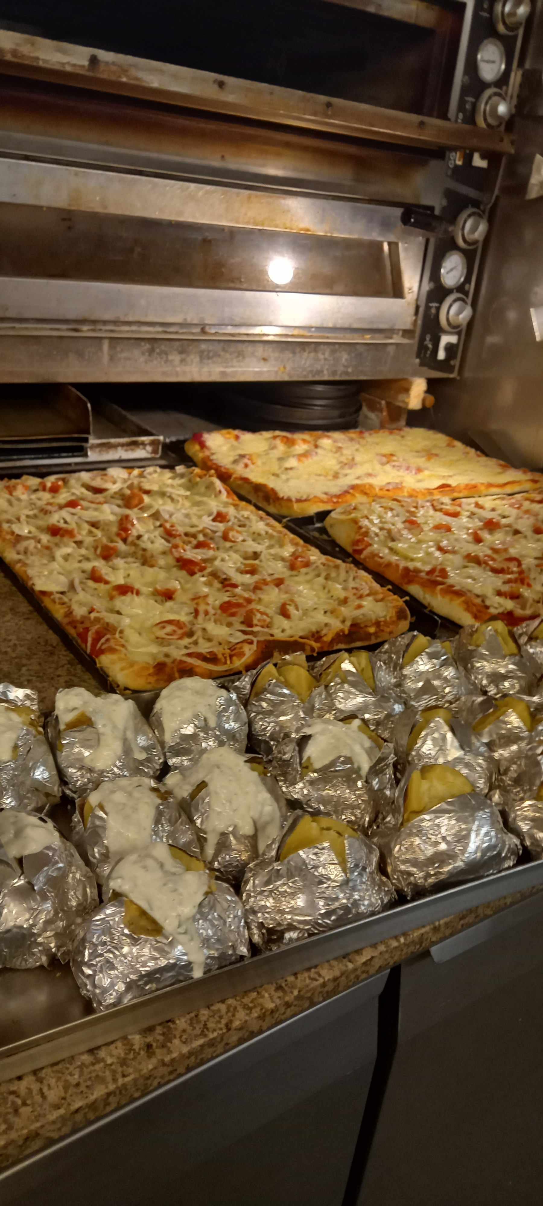 In einem Ofen werden drei Pizzen und Kartoffeln gebacken. Leonardo Intelisano Pizzeria Dolce Vita