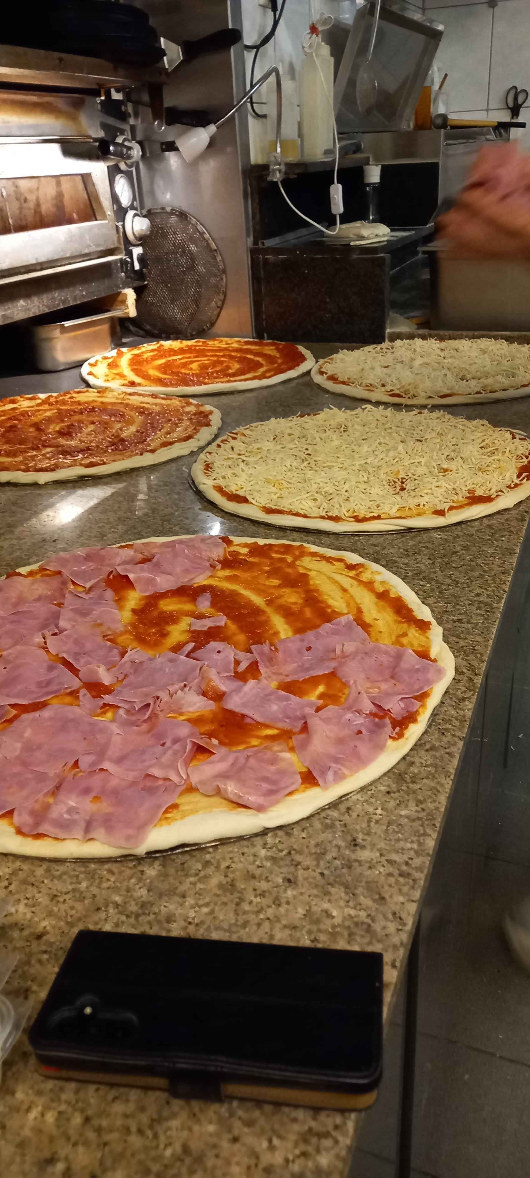 Mehrere Pizzen sind auf einer Theke aufgereiht mit unterschiedlichen Belägen, Leonardo Intelisano Pizzeria Dolce Vita