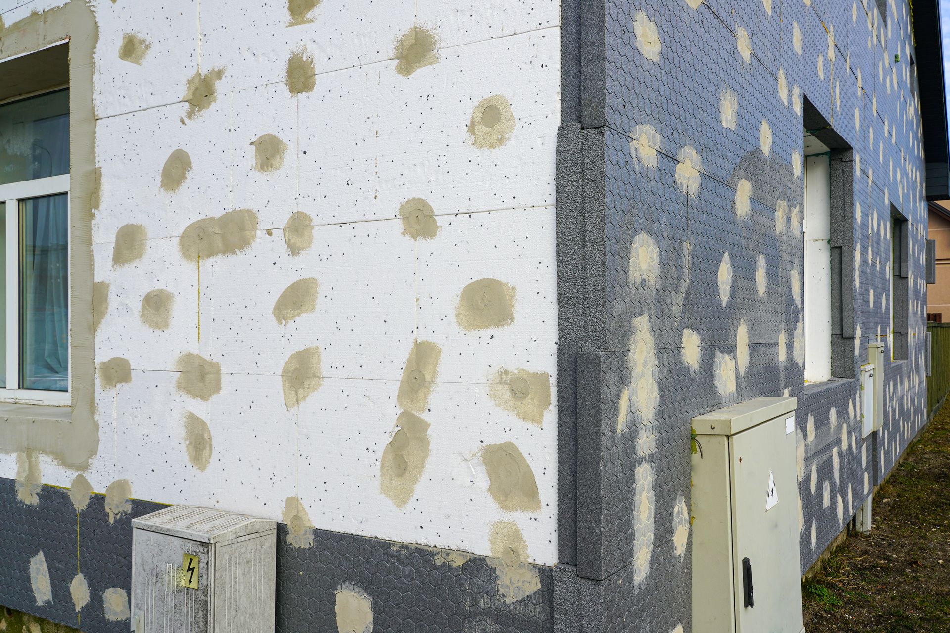 Mur extérieur avec isolation en mousse blanche, ciment gris et boîtes électriques.