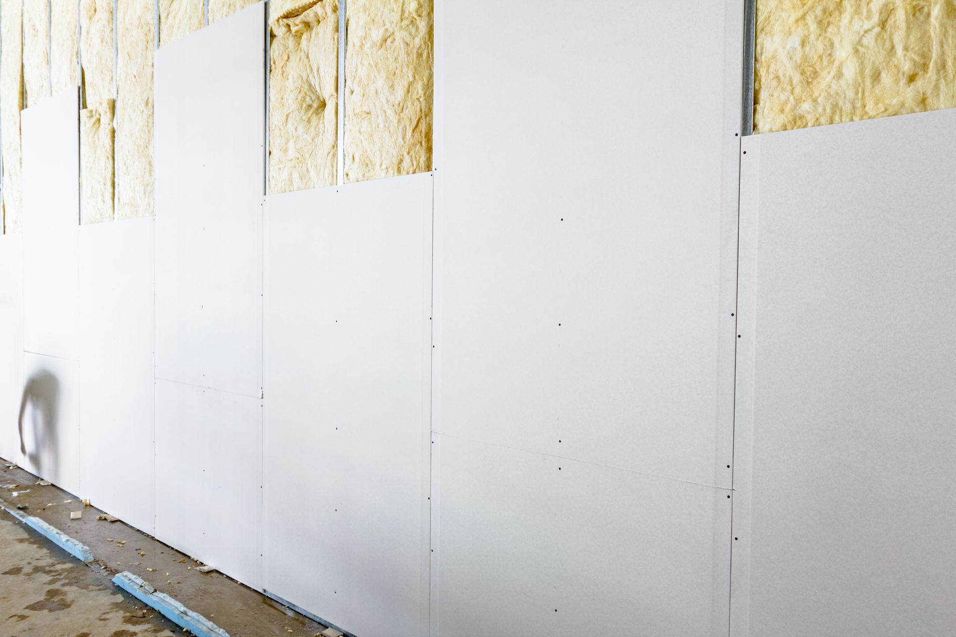 Mur intérieur en construction : panneaux de cloison sèche blancs fixés sur des montants métalliques, isolation exposée.