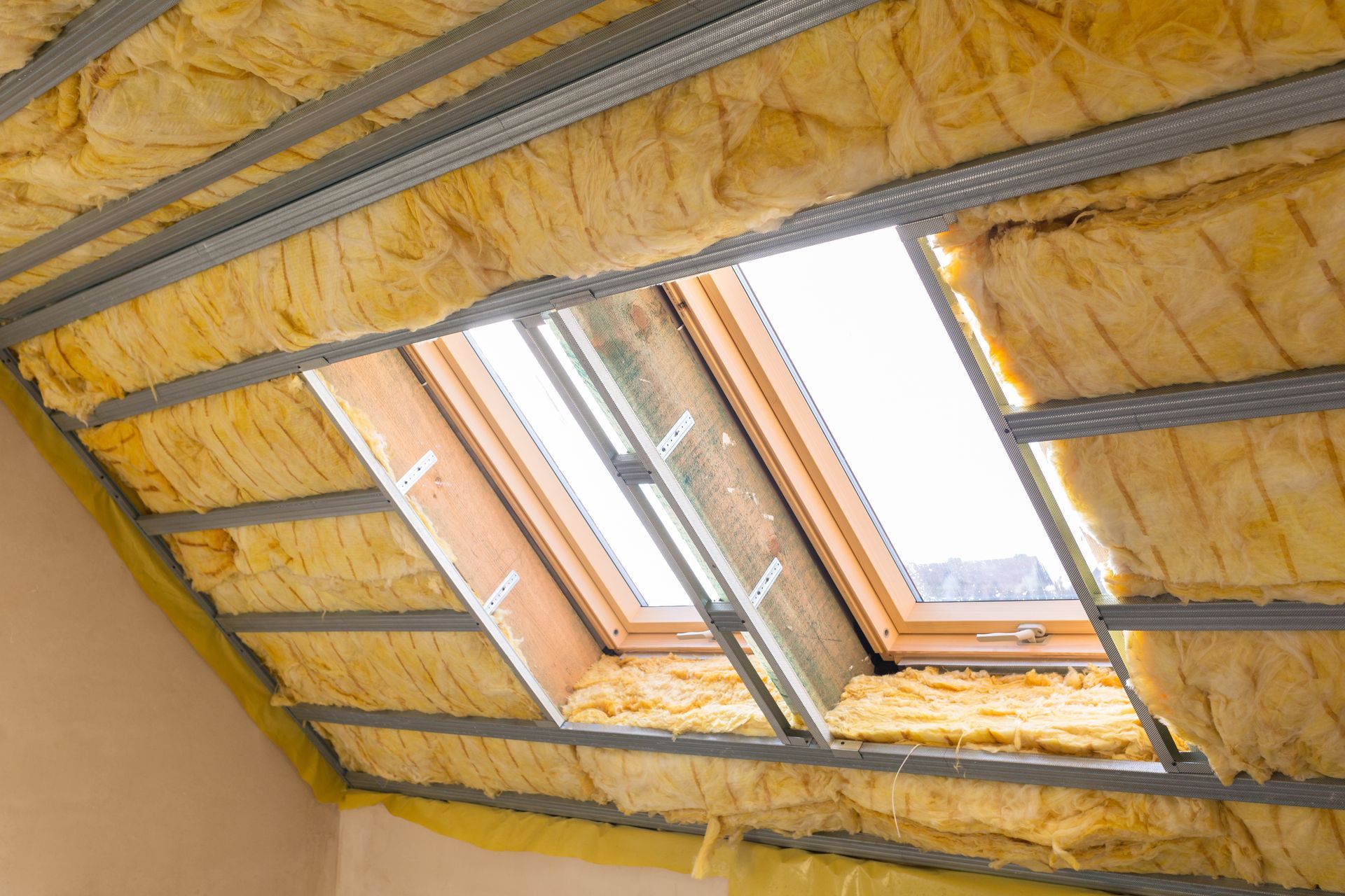 Plafond mansardé avec isolation jaune, charpente métallique et puits de lumière.