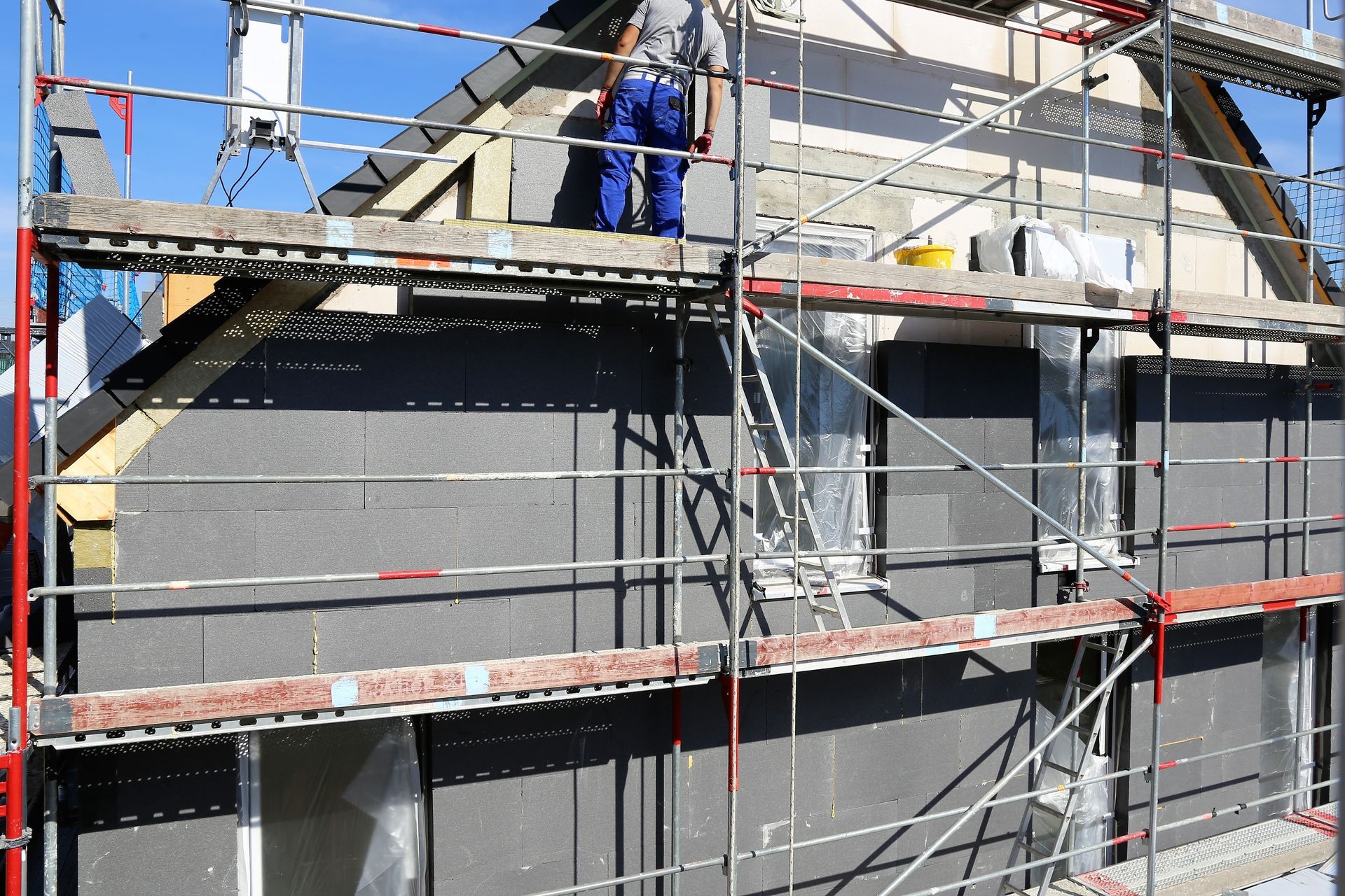 Ouvrier du bâtiment sur un échafaudage installant des panneaux isolants gris sur l'extérieur d'une maison.