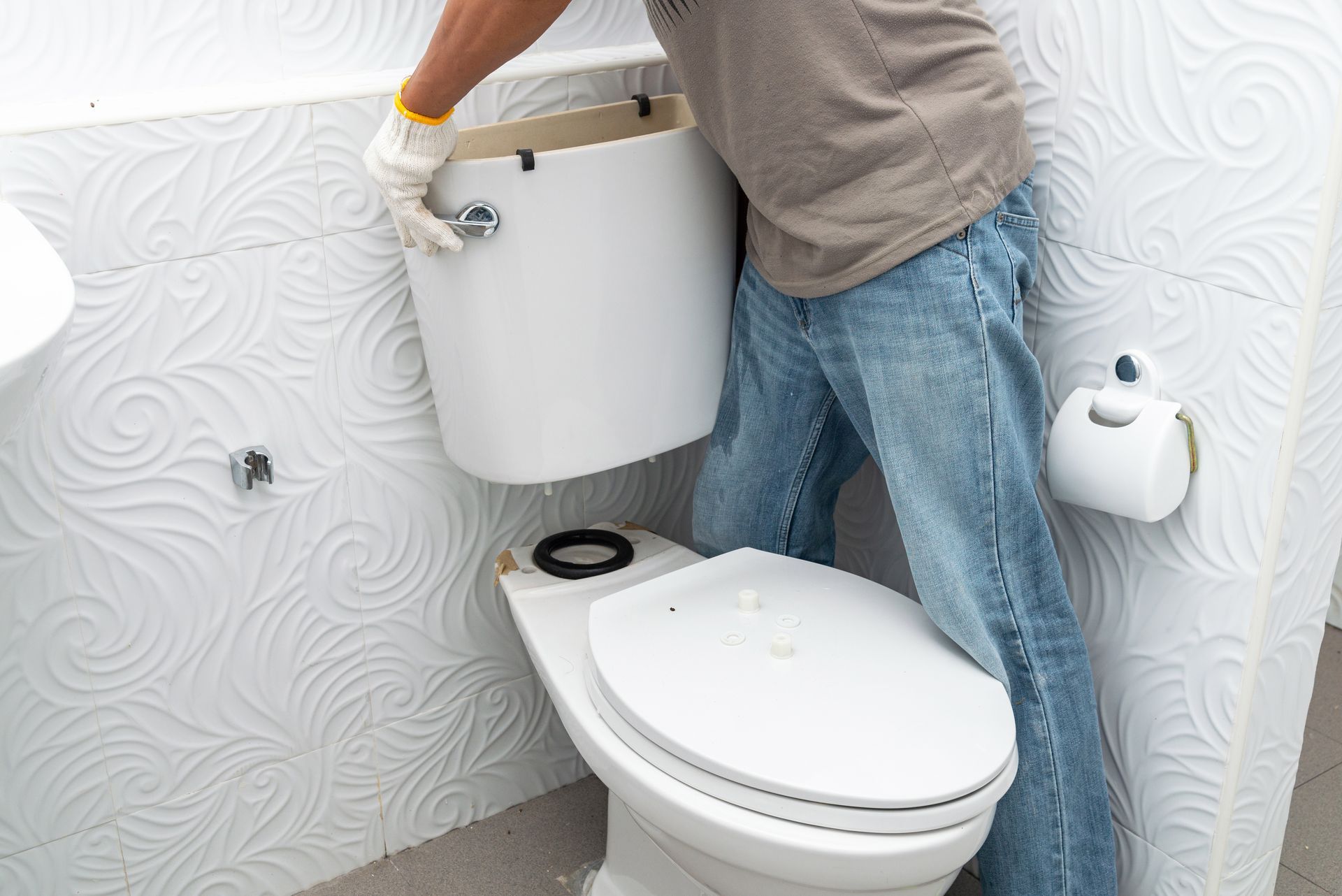 Personne installant un réservoir de toilette sur la cuvette d'une salle de bains.