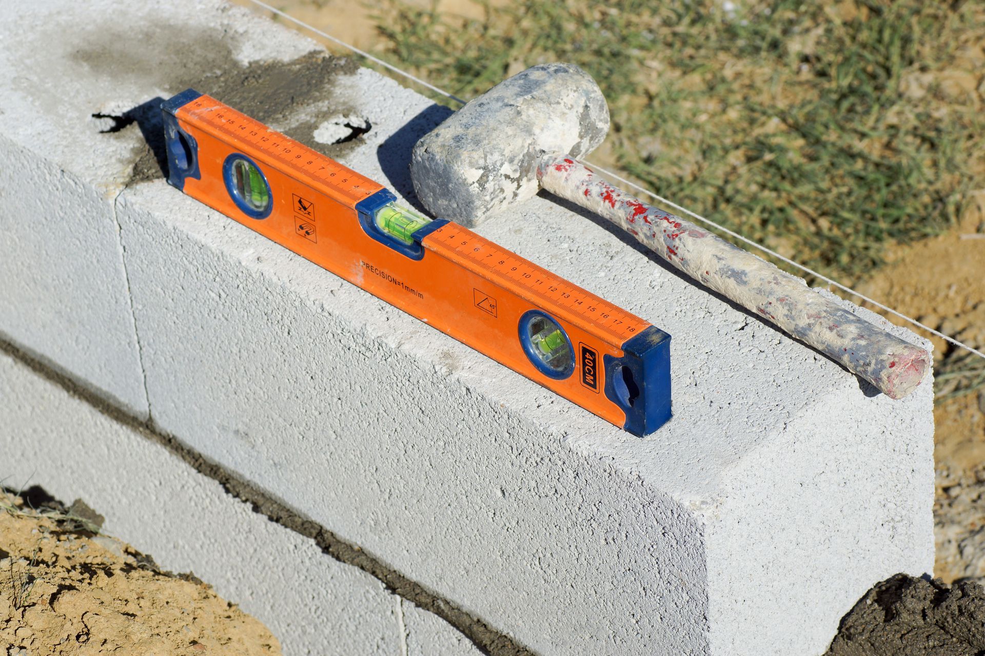Niveau orange et maillet posés sur un mur en parpaings, mortier visible. Extérieur.