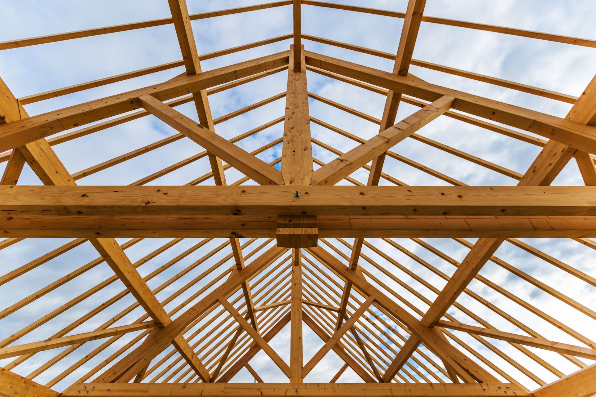 Charpente de toit en bois contre un ciel nuageux, montrant des poutres, des chevrons et des supports structurels.
