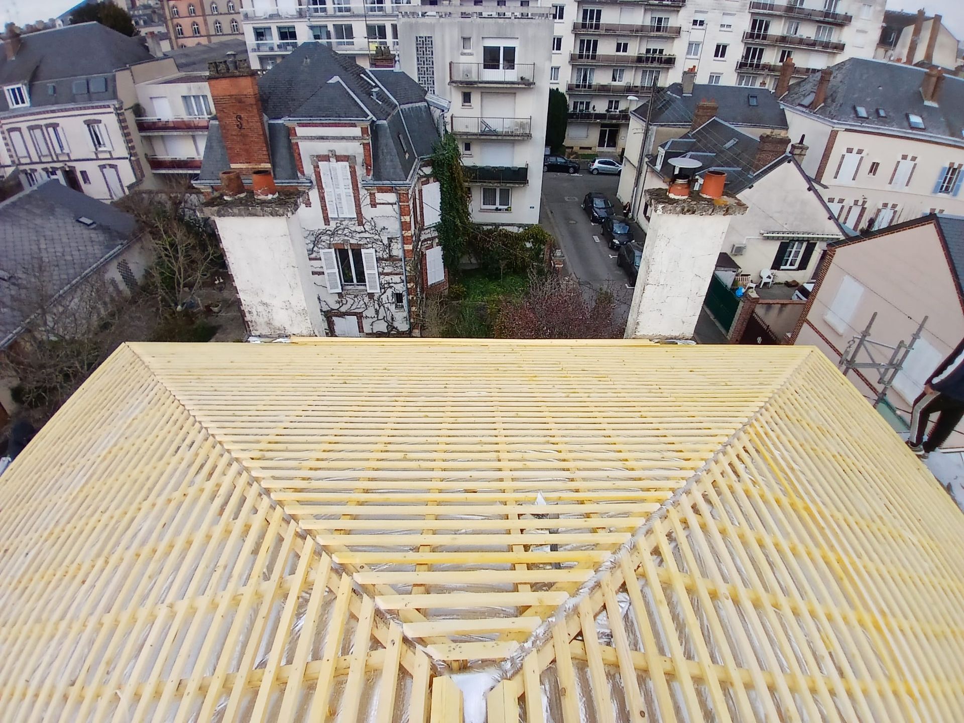 Toiture en bois en construction, vue en angle des poutres et de la charpente. Bâtiments et rue en arrière-plan.