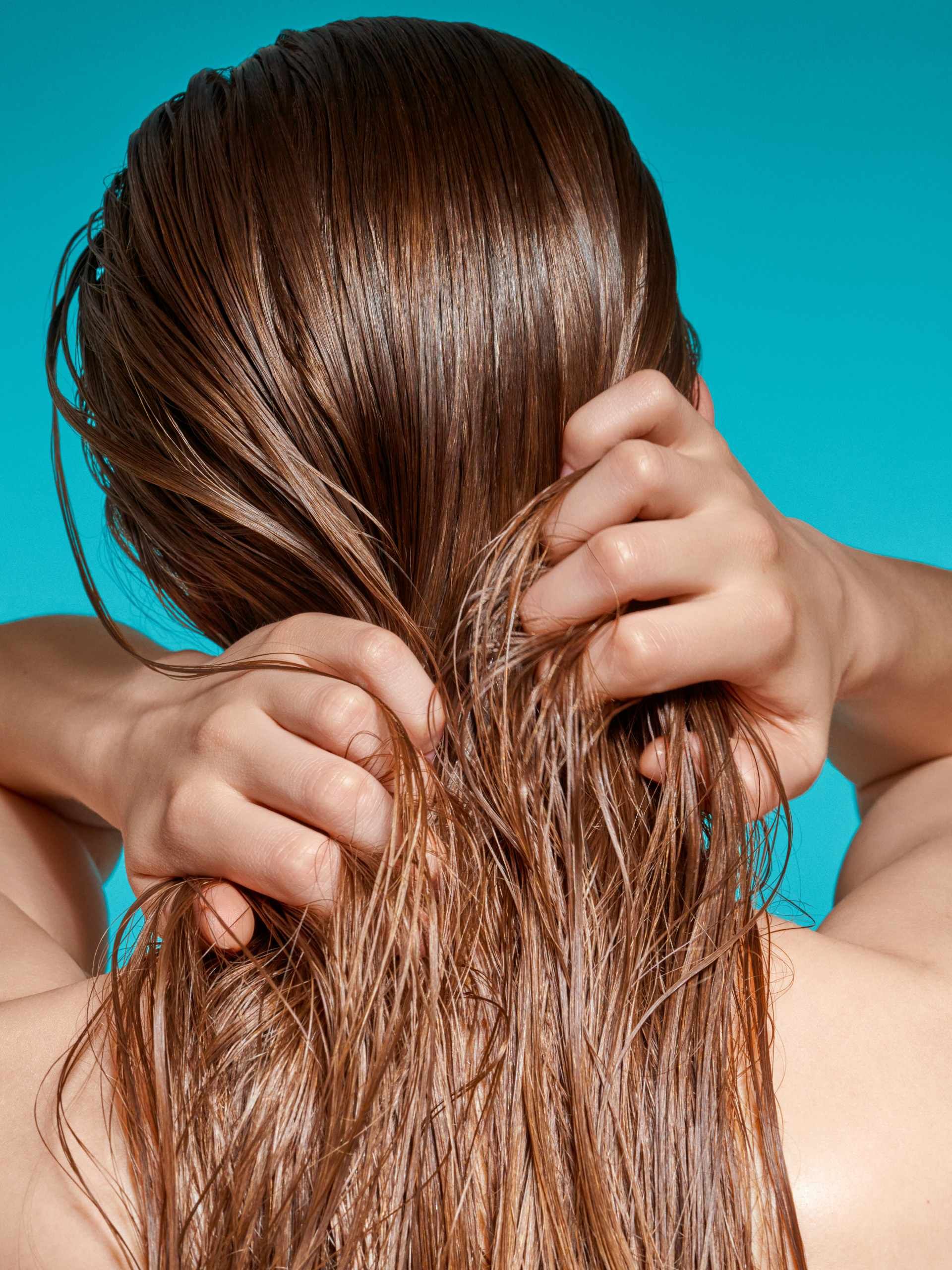 Frau trägt Pflegeprodukte auf ihr Haar auf und arbeitet sie mit den Fingern ein