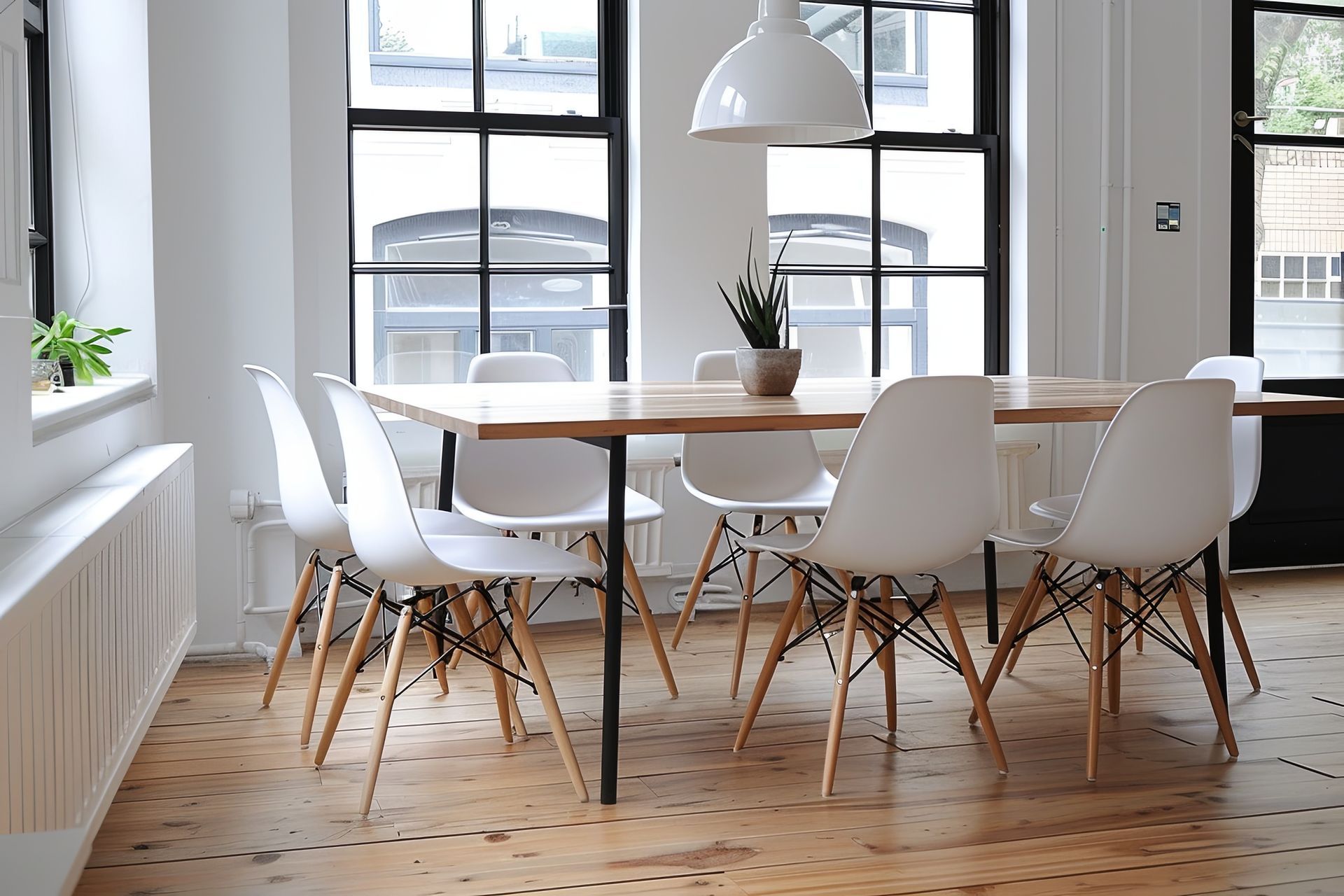 Salle à manger avec table en bois et six chaises blanches ; suspension lumineuse au plafond ; grandes fenêtres.