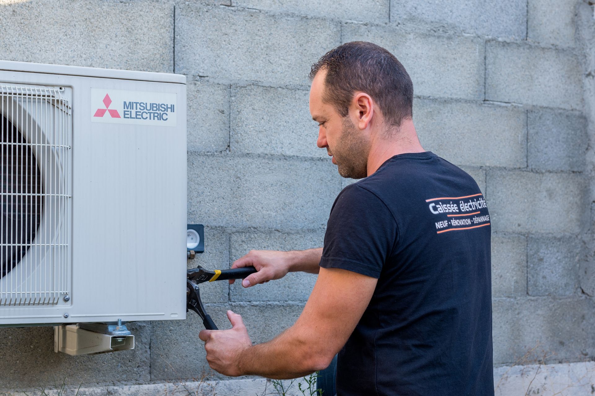 Artisan de Caissée Électricité installant qui fixe une pompe à chaleur