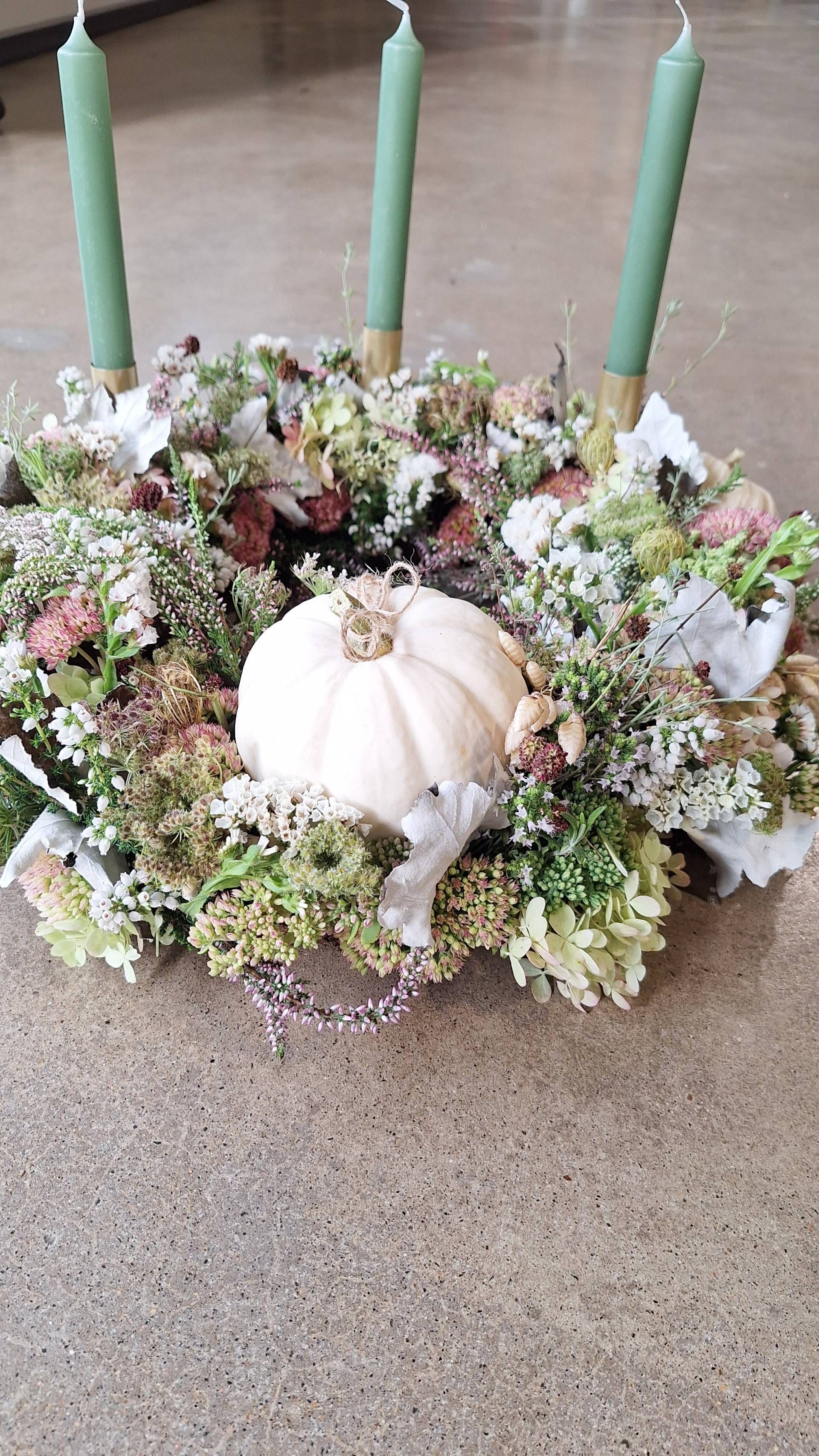 Kranz aus verschiedenen getrockneten Blumen in Gelb, Weiss und Lila auf einem Holzsockel.