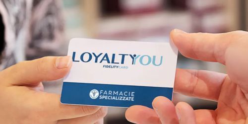 In un negozio, una persona porge a un'altra una tessera fedeltà della farmacia di colore bianco e blu con la scritta 