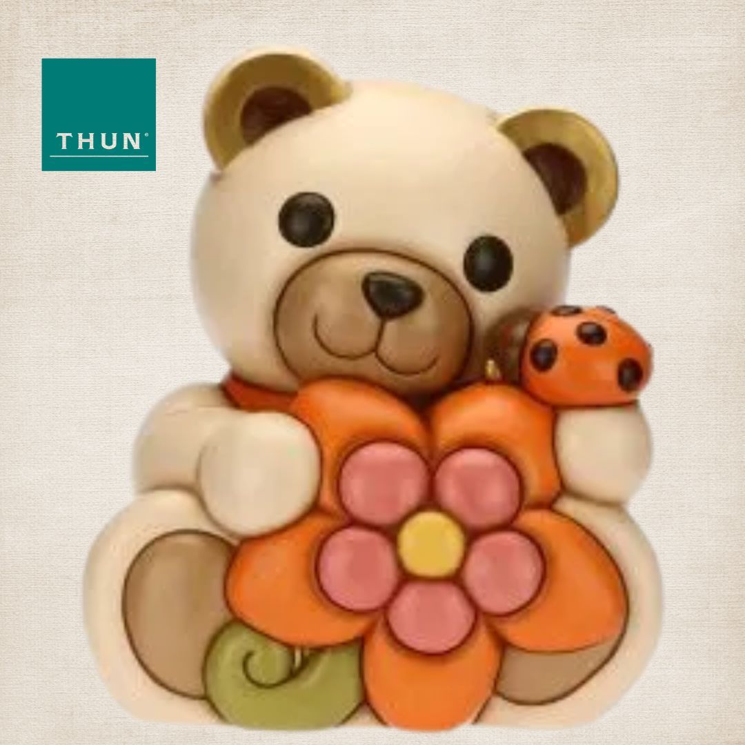 Classico orsetto in ceramica della Thun, colore beige che abbraccia un fiore arancione con sopra una coccinella