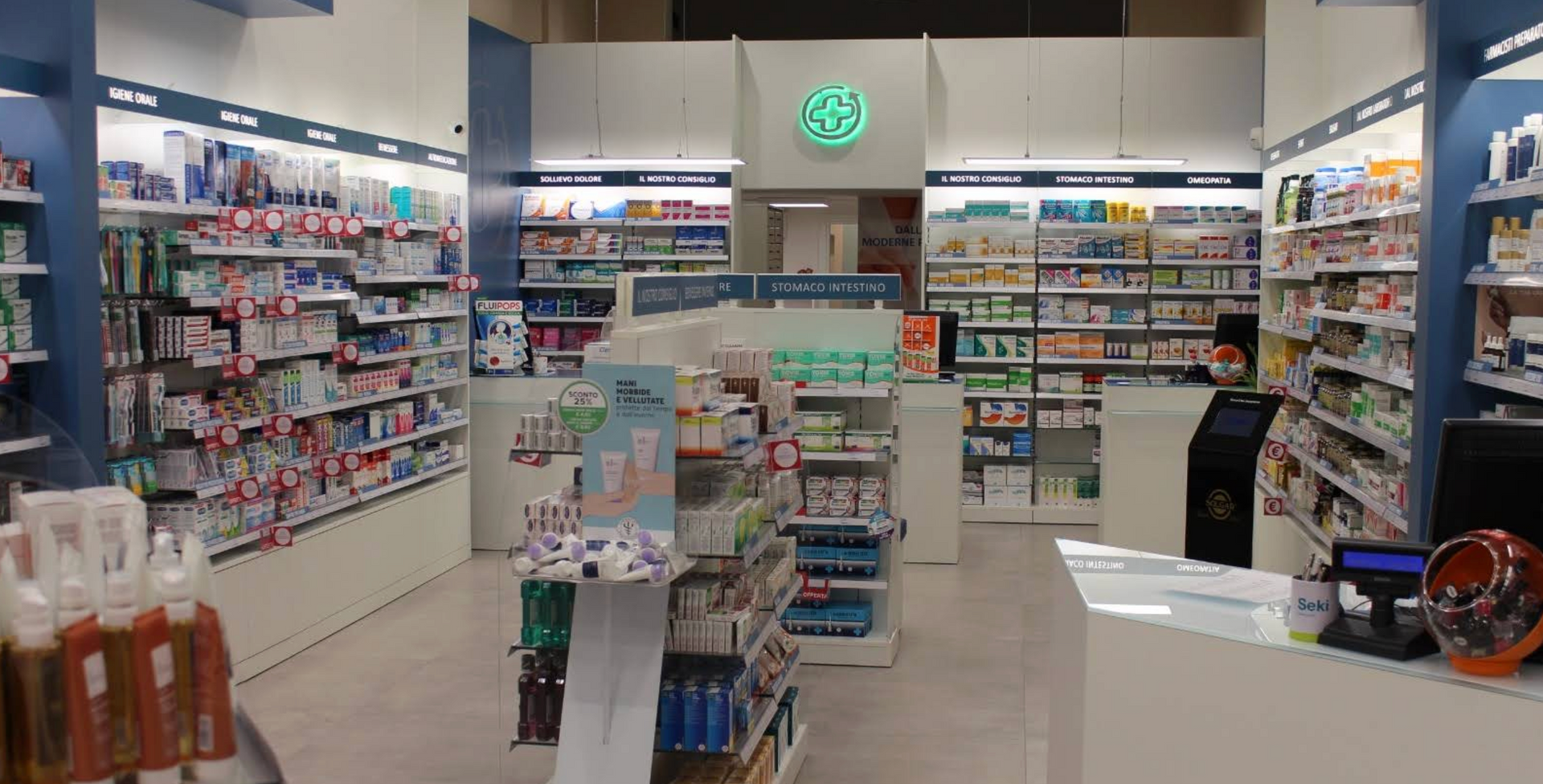 L'interno di una farmacia ben illuminata, con scaffali pieni di vari prodotti per la salute e la bellezza e un bancone per il pagamento.