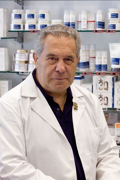 Una persona in camice bianco è in piedi davanti a degli scaffali pieni di vari prodotti per la cura della pelle e farmaci.