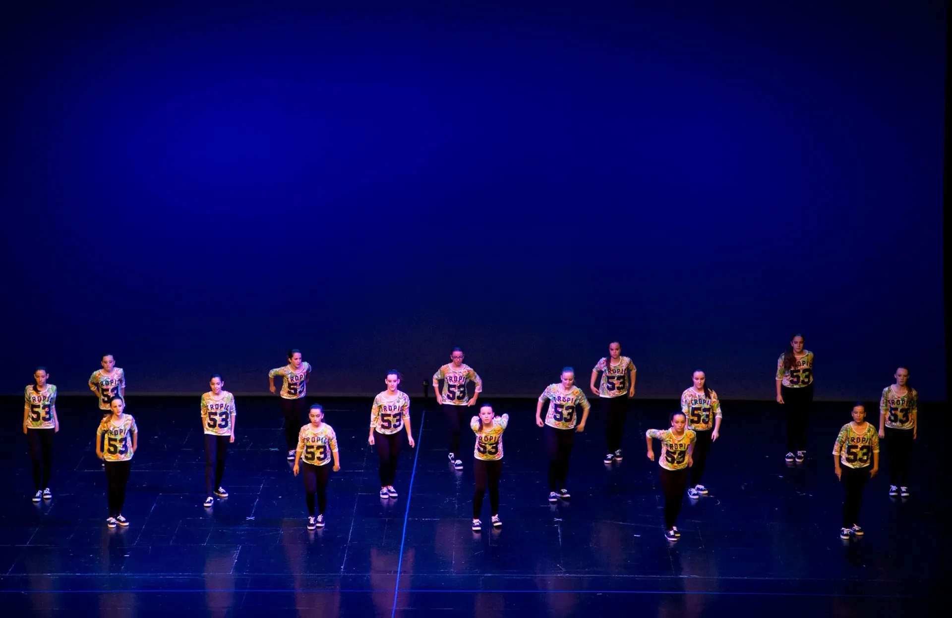 Un grup de persones balla en un escenari amb fons blau.