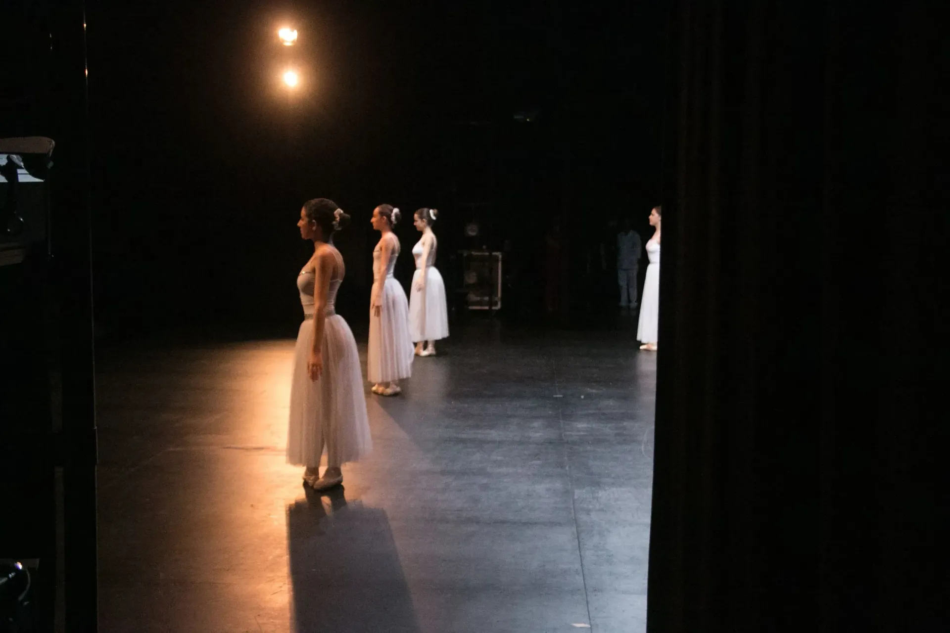Un grup de ballarines està dret en un escenari en una habitació fosca.