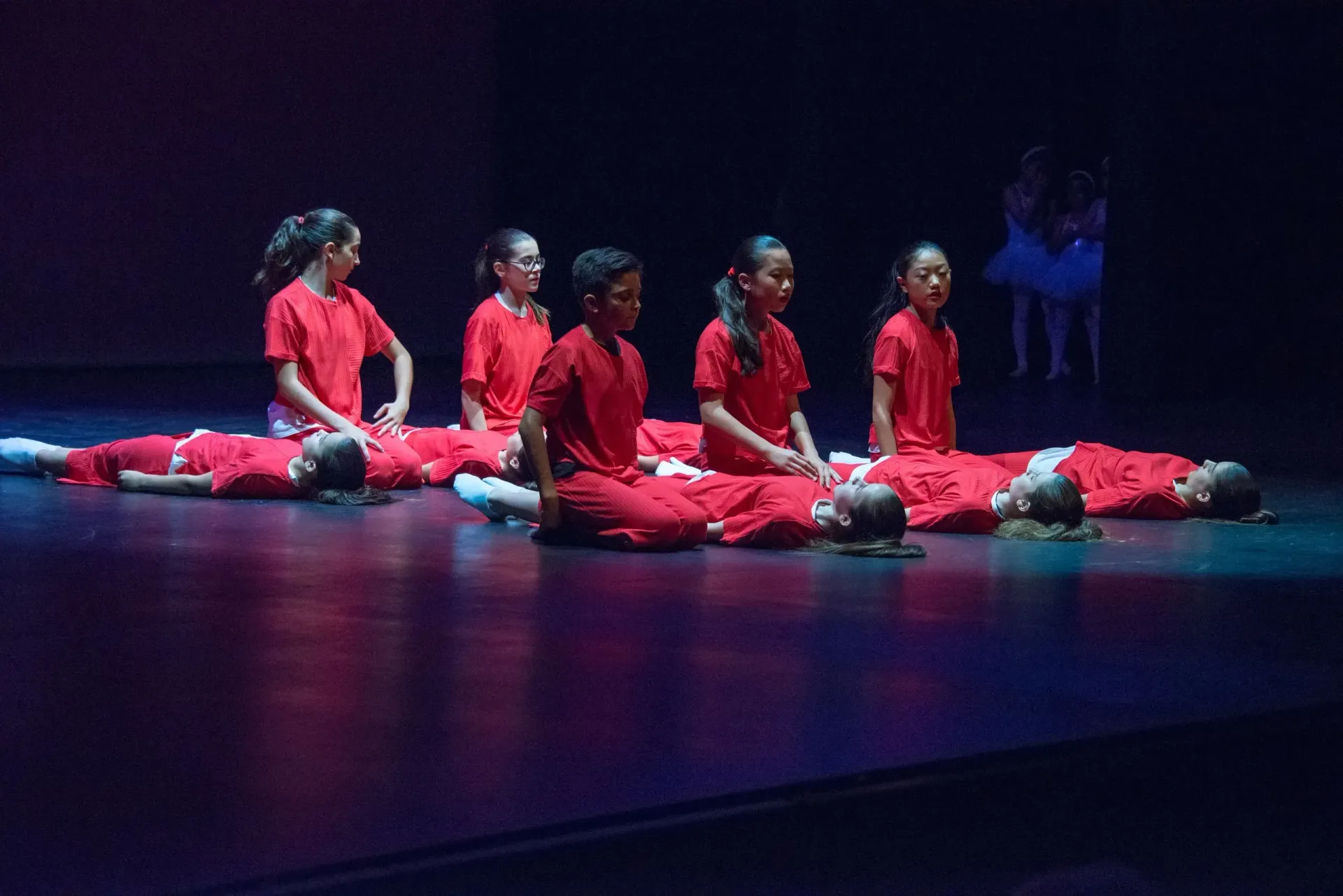 Un grup de noies joves amb camises vermelles estan estirades a terra en un escenari.