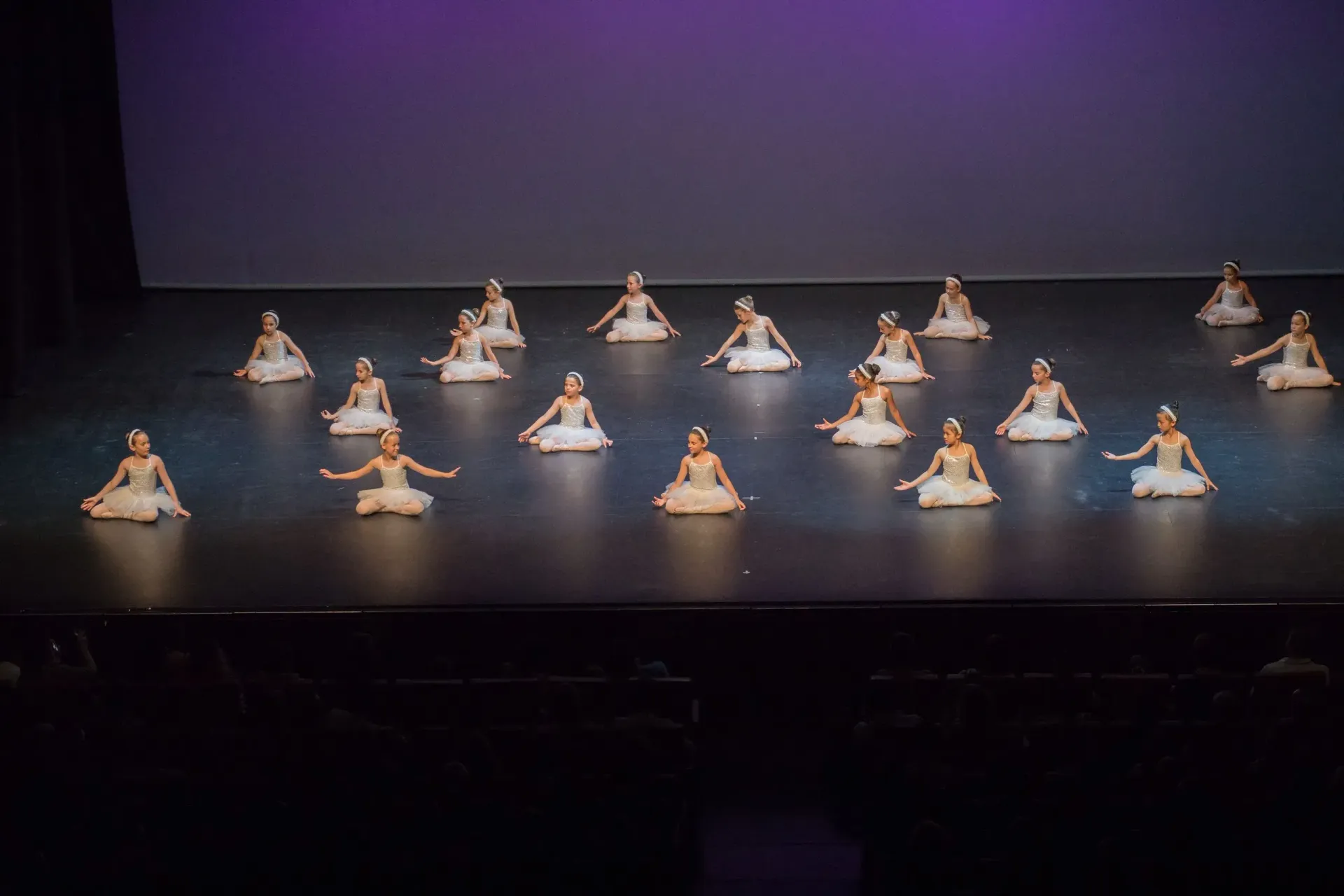 Un grup de ballarins estan asseguts a terra en un escenari.
