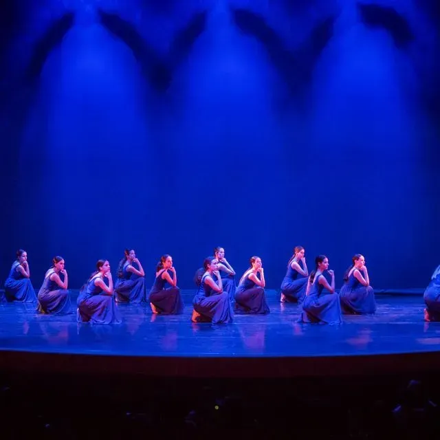 Un grupo de mujeres está sentada en un escenario frente a un fondo azul.
