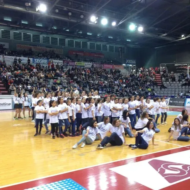 Un gran grup de persones estan reunides en una pista de bàsquet amb la lletra s a terra