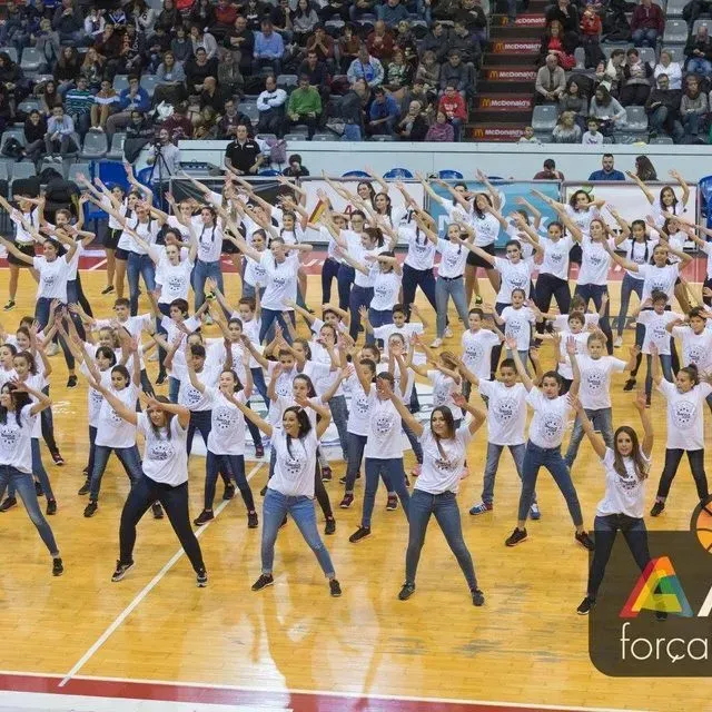 Un gran grup de persones ballant en una pista de bàsquet amb la paraula força a la cantonada
