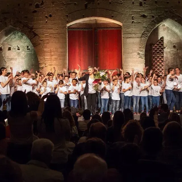 Un grup nombrós de persones està dret en un escenari amb les mans enlaire.