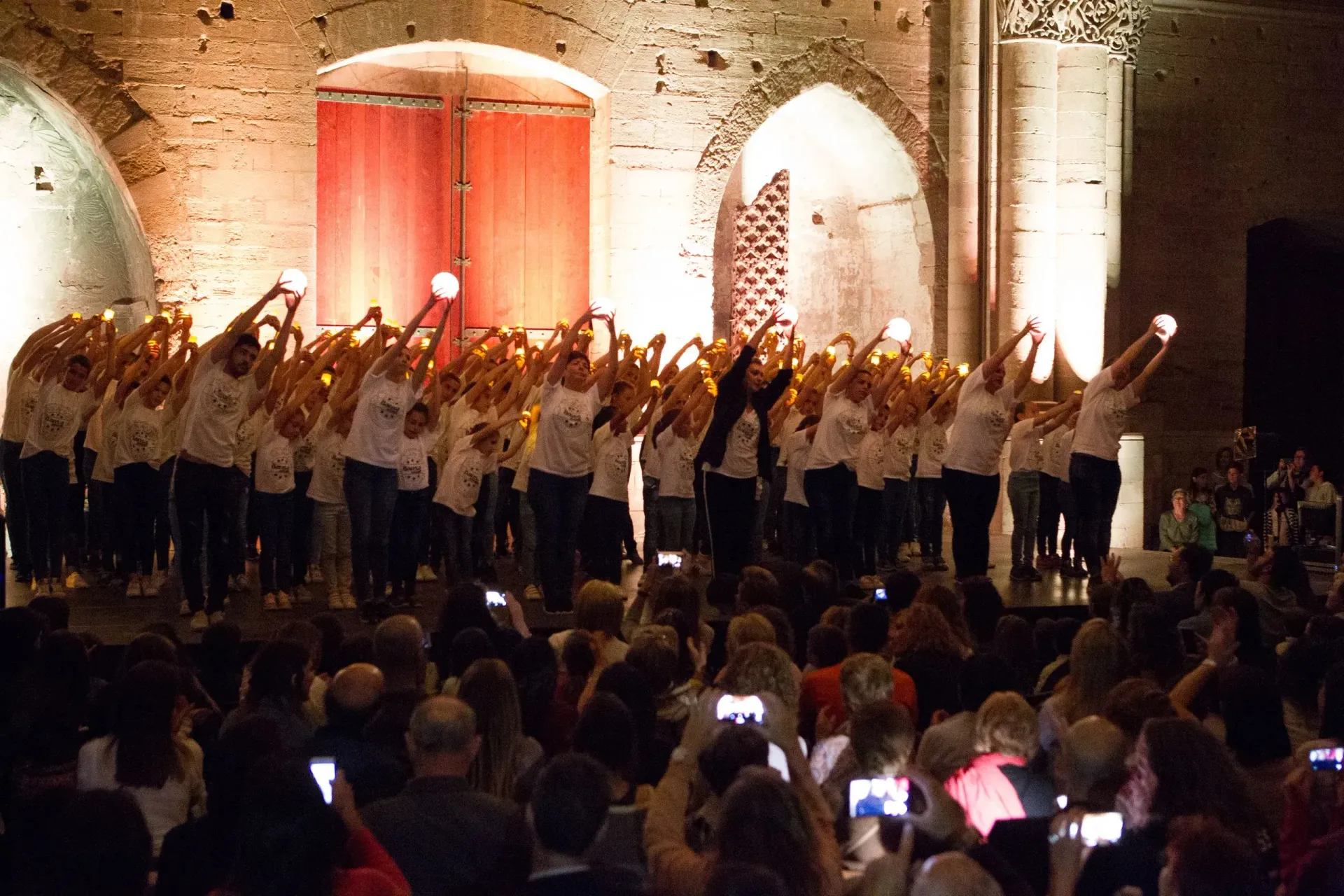 Un grup nombrós de persones està dret en un escenari amb espelmes a les mans.