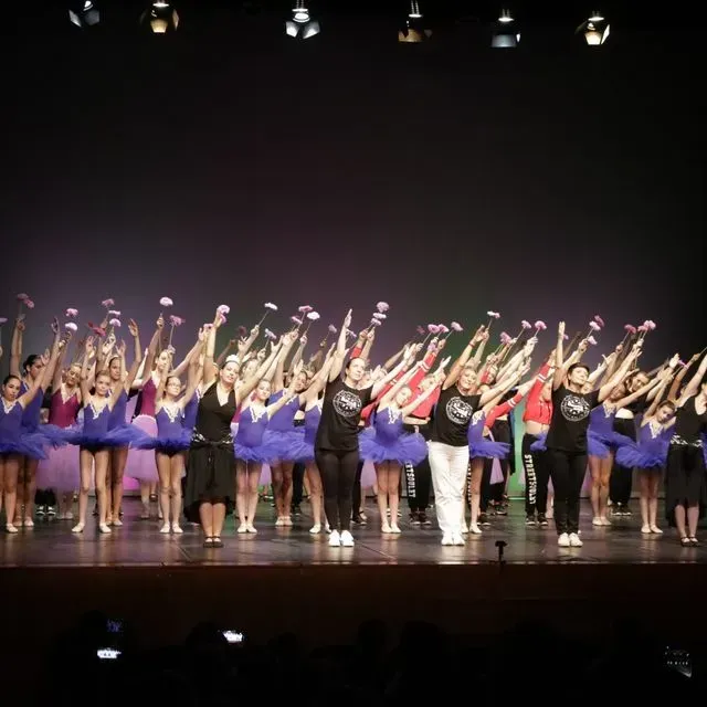 Un gran grup de persones estan dretes en un escenari amb els braços enlaire