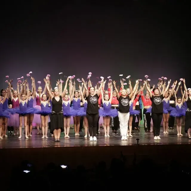 Un gran grup de persones estan dretes en un escenari amb els braços enlaire