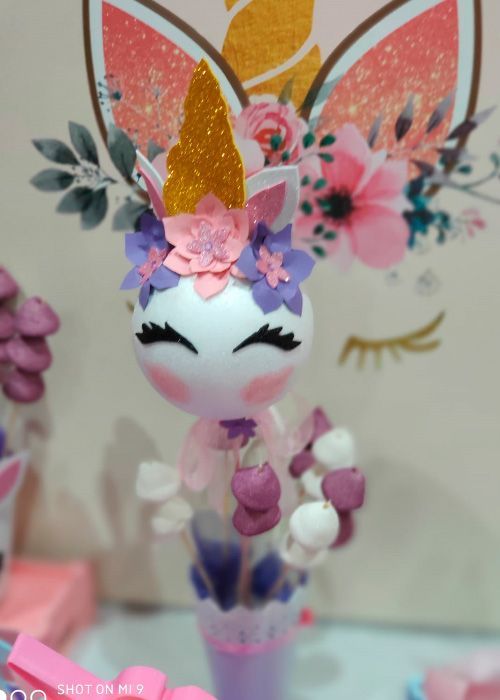 Una muñeca unicornio con flores en la cabeza está sentada en una mesa.
