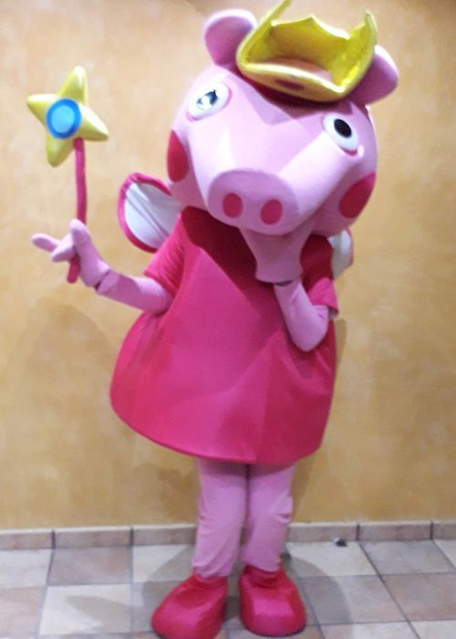 Una mascota de cerdo rosa sostiene una varita y lleva una corona.