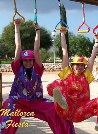 Dos chicas con disfraces de fiesta mallorquina se columpian en barras de mono.