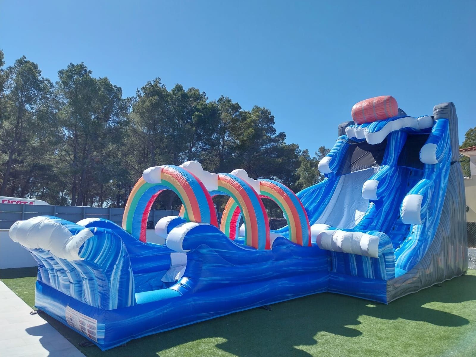 Un gran tobogán de agua inflable con un arcoíris encima se encuentra sobre un exuberante campo verde.