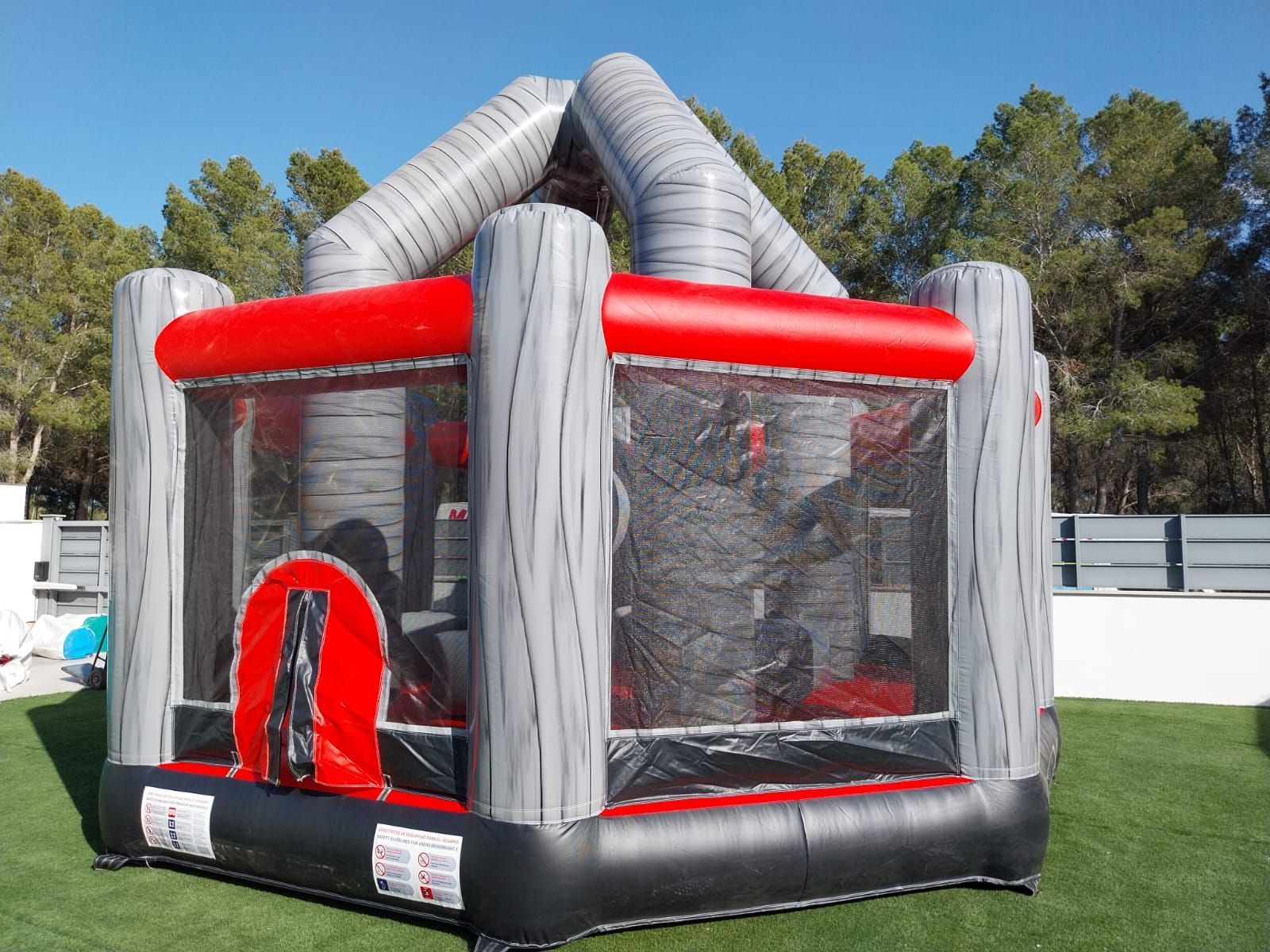Una casa inflable gris y roja se encuentra en la parte superior de un exuberante campo verde.