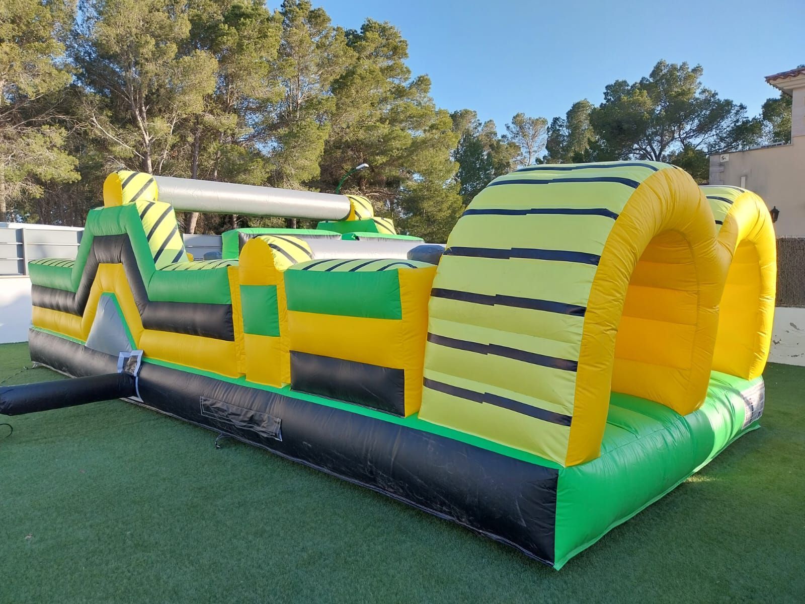 Una carrera de obstáculos inflable verde y amarilla se encuentra sobre un exuberante campo verde.