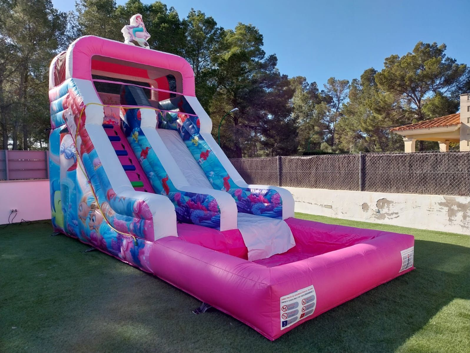Un tobogán de agua inflable rosa y azul se encuentra sobre un exuberante campo verde.