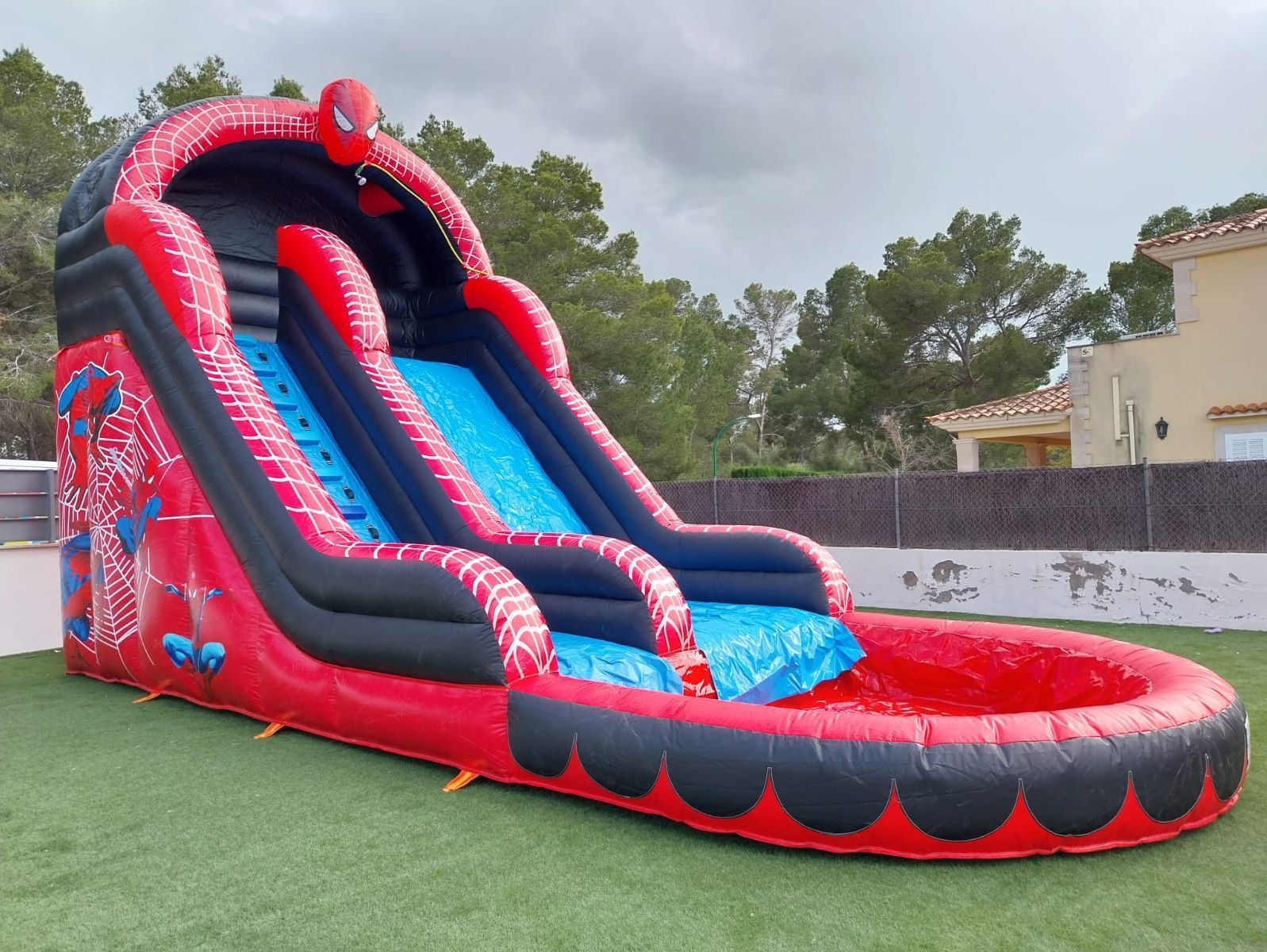 Un tobogán de agua inflable con forma de Spiderman se encuentra sobre un exuberante campo verde.
