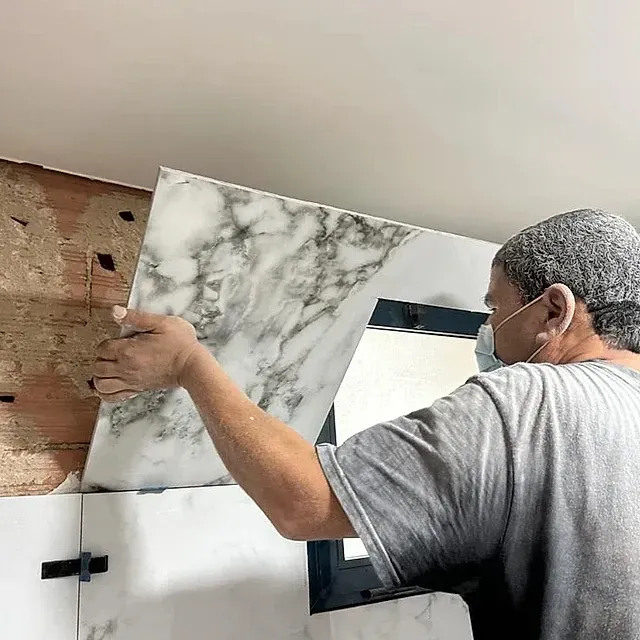 Un hombre que lleva una máscara sostiene un trozo de mármol en una pared.