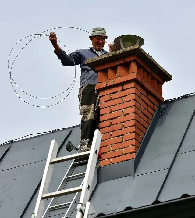 Un hombre de pie en lo alto de una escalera junto a una chimenea de ladrillo.