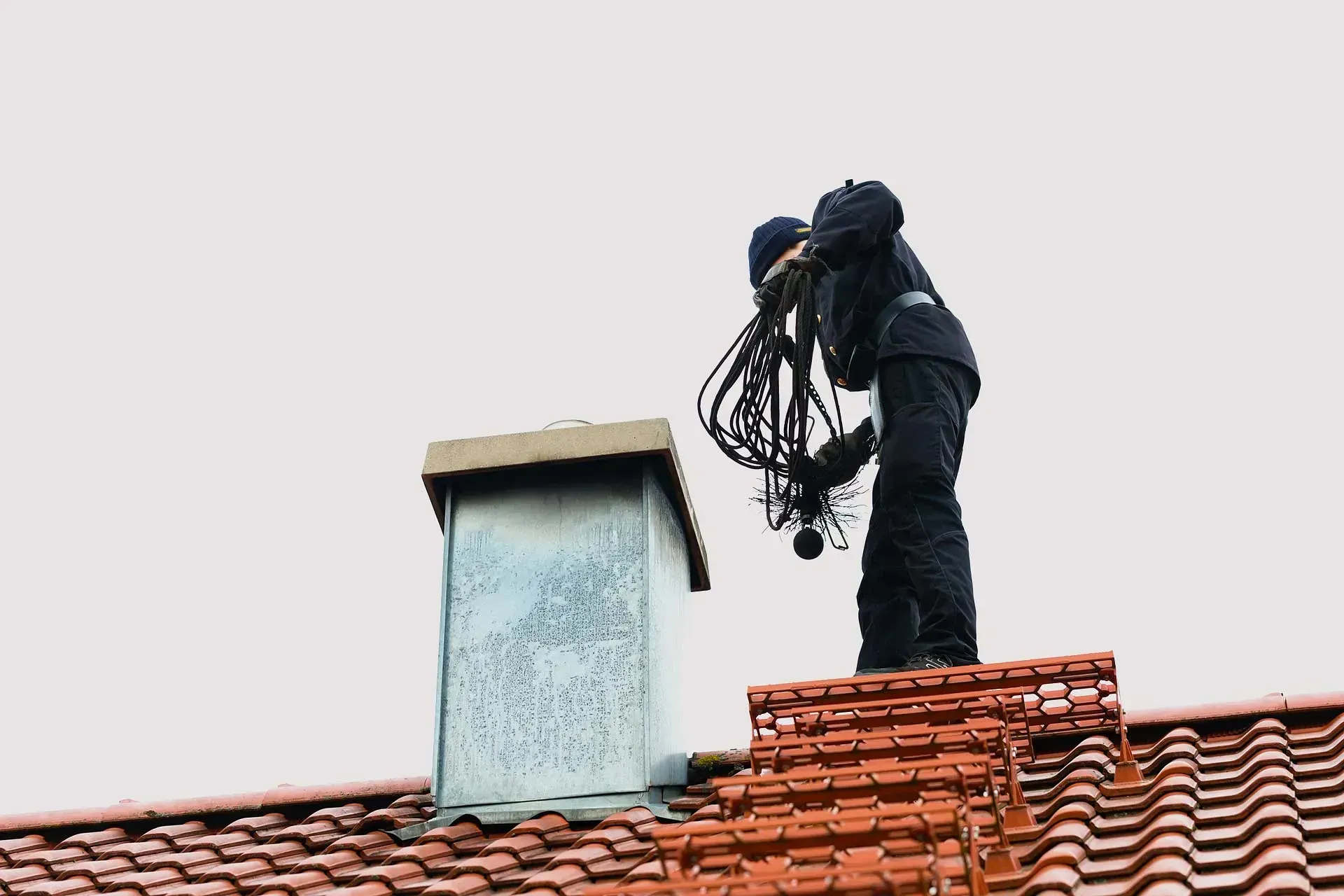 Un hombre está de pie encima de un tejado limpiando una chimenea.