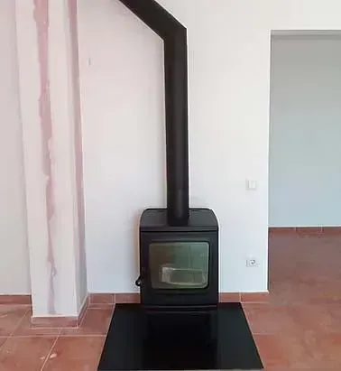 Una estufa de leña negra está ubicada en una sala de estar junto a una pared.