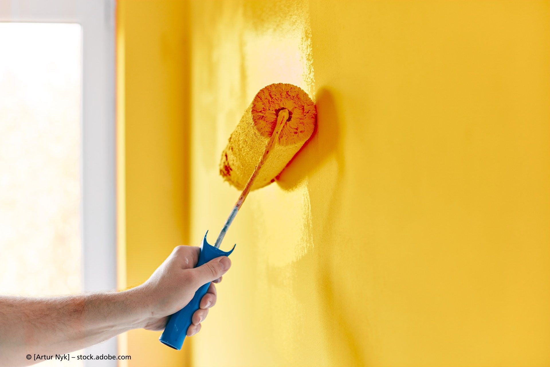 Eine Person streicht mit einer Farbrolle eine gelbe Wand.