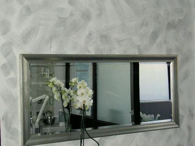 Ein Spiegel an einer Wand mit einer Vase mit Blumen davor