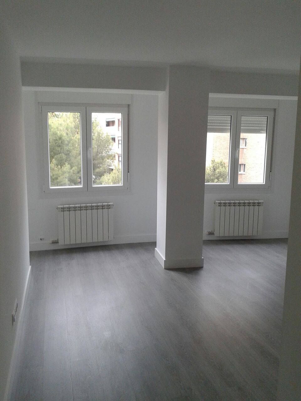 Una gran habitación vacía con muchas ventanas y radiadores.